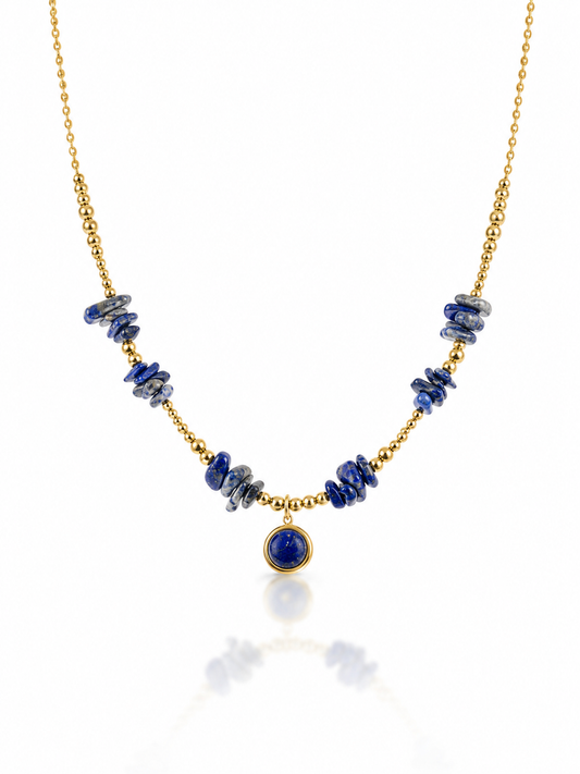 A gold chain necklace featuring irregular dark blue lapis lazuli stone chips on either side of a central round blue stone pendant, displayed on a clean white background with a soft reflection.
