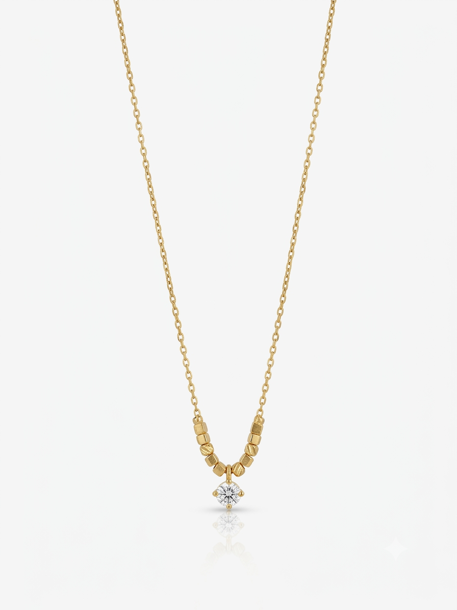 A delicate yellow gold chain necklace featuring a small cluster of textured gold beads leading to a single round-cut clear gemstone pendant, displayed against a light gray background.