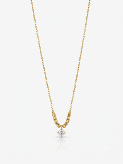 A delicate yellow gold chain necklace featuring a small cluster of textured gold beads leading to a single round-cut clear gemstone pendant, displayed against a light gray background.